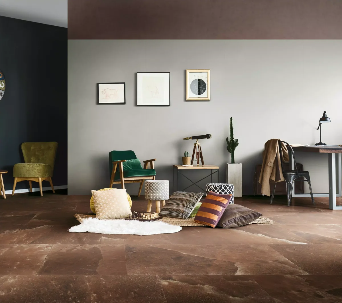 Woonkamer met een roodbruine vloer in grootformaat, een groene fauteuil, kussens op een vloerkleed en een grijs wandvlak zonder zichtbare naden
