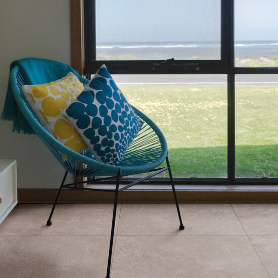 Turquoise draadstoel met gedessineerde kussens bij een groot raam, op een betonlook vloer in een warme zandtint