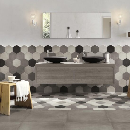 Badkamer met een wand vol hexagontegels in grijstinten, twee zwarte waskommen op een houten meubel en een grijze betonlookvloer