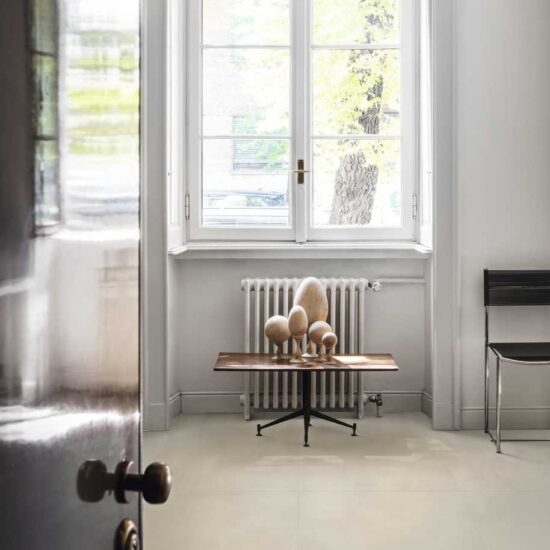 Lichte betonlookvloer binnen bij een openslaande deur, met een raam, een radiator en een klein bijzettafeltje