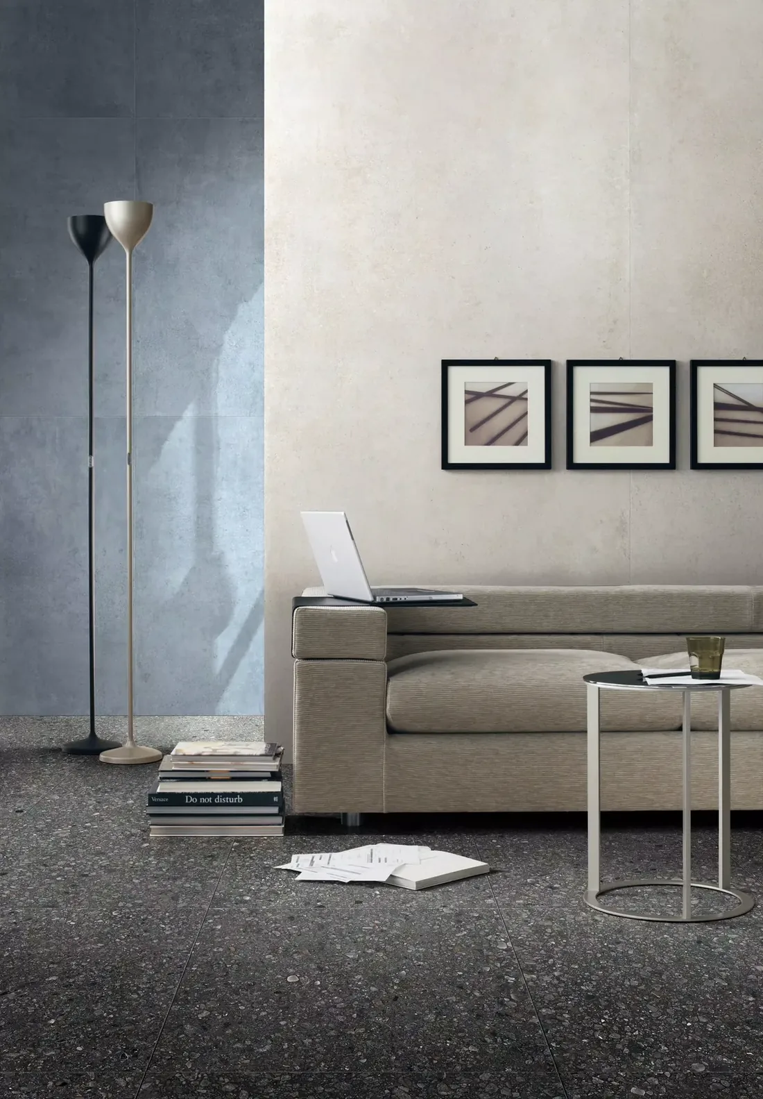 Woonkamer met een donkere, gespikkelde betonlookvloer, een lage bank en drie lijsten aan de wand