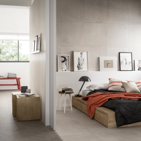 Slaapkamer met een zandkleurige betonlookwand in grootformaat, een houten bed met oranje plaid en een lichte vloer