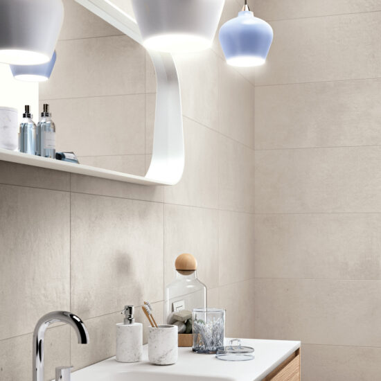 Badkamer met bleke betonlooktegels, een wastafel met spiegel en drie hanglampen