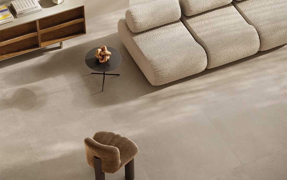 Woonkamer van boven gezien, met een bleke greige betonlookvloer, een bank en een fauteuil