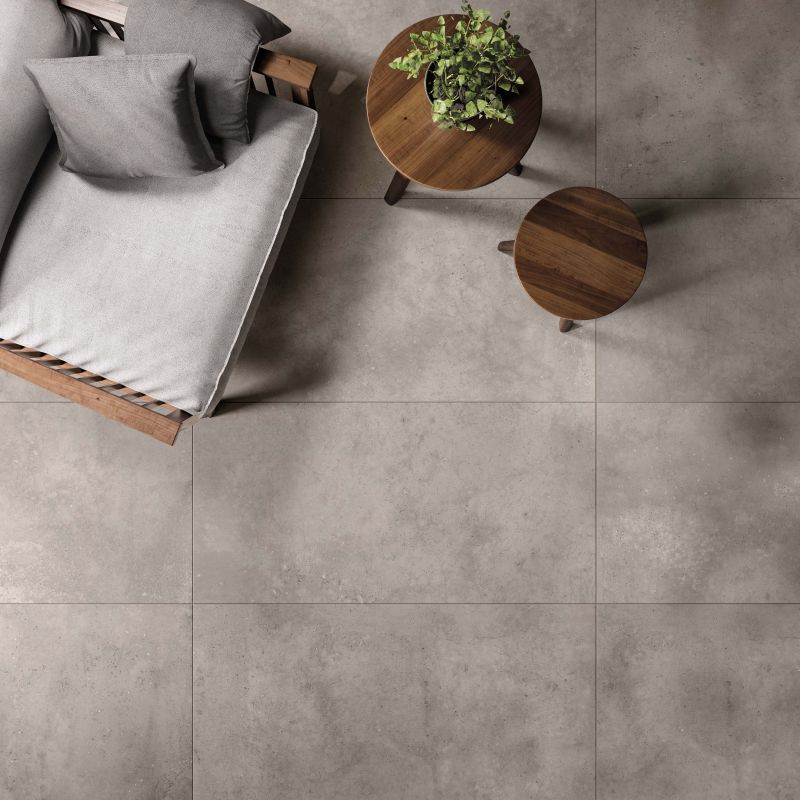 Bovenaanzicht van een grijze betonlookvloer in betonoptiek, met een daybed en twee ronde houten tafeltjes
